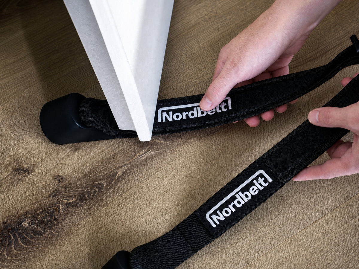 Hände schieben einen Nordbelt-Gurt unter eine offene weiße Tür auf einem Holzboden.