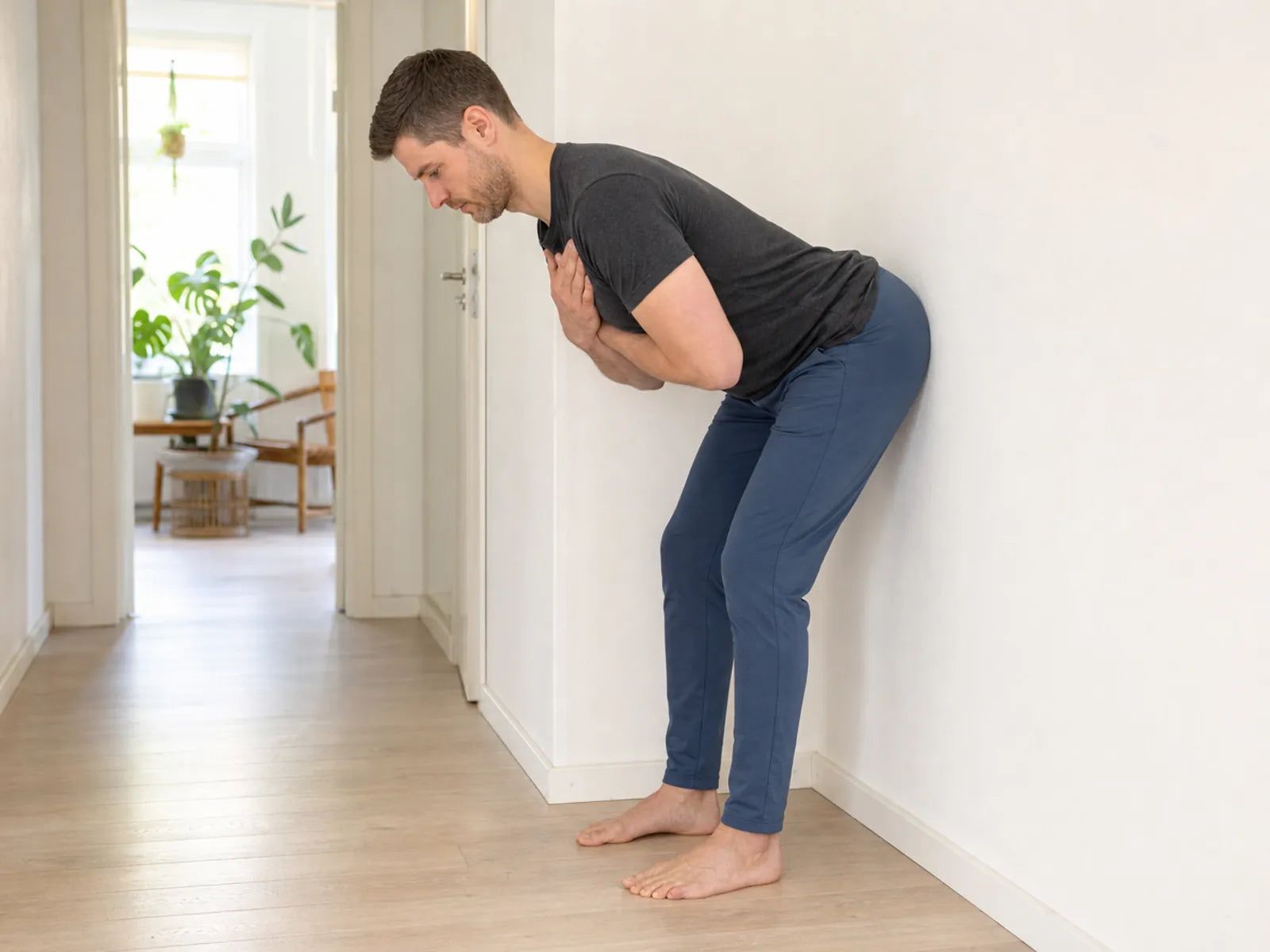 Erwachsener Mann nutzt bei einer Good-Morning-Übung für die Hamstrings einen Wall Tap.