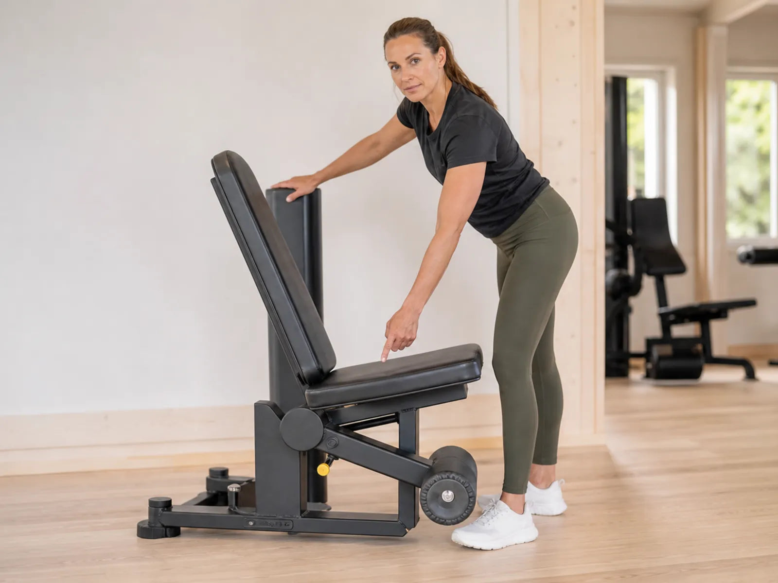 Beim Einstellen einer Leg-Curl-Maschine für die Hamstrings kontrolliert eine erwachsene Frau Sitz und Rollenposition.