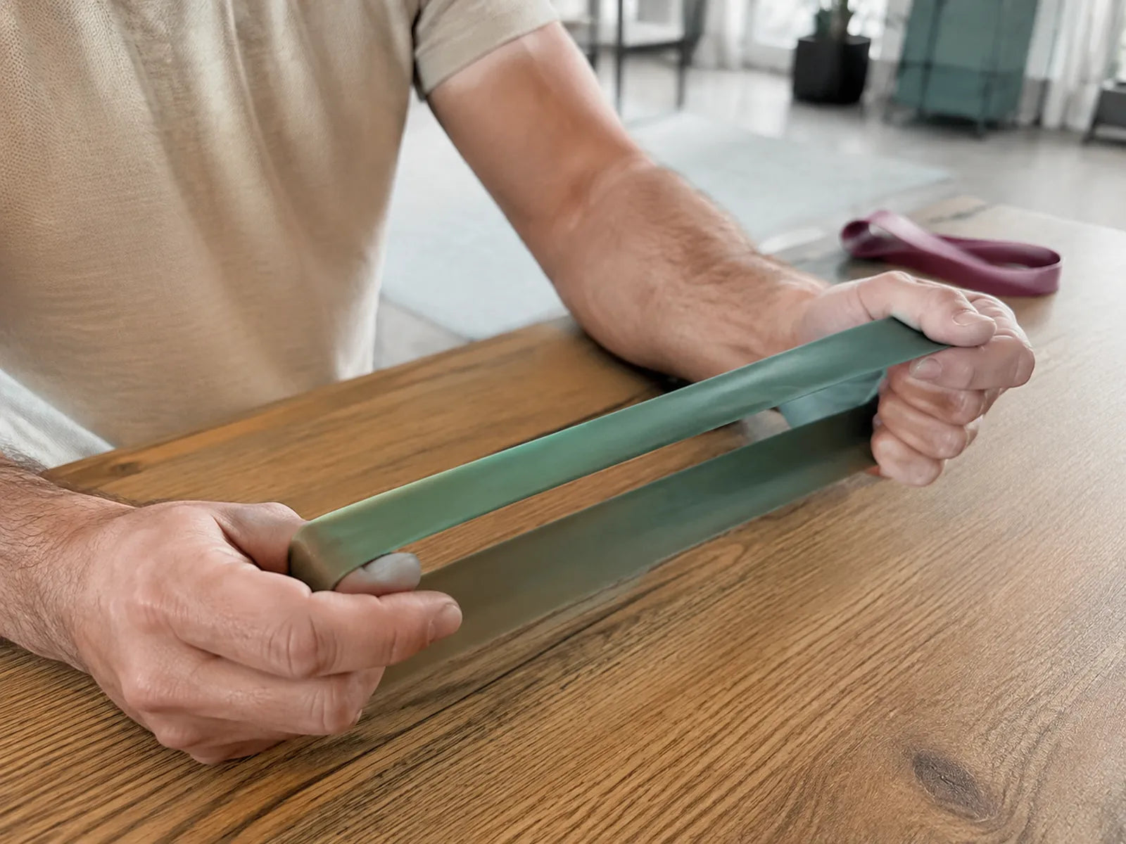 Hands stretch a green rubber exercise loop above a wooden table.