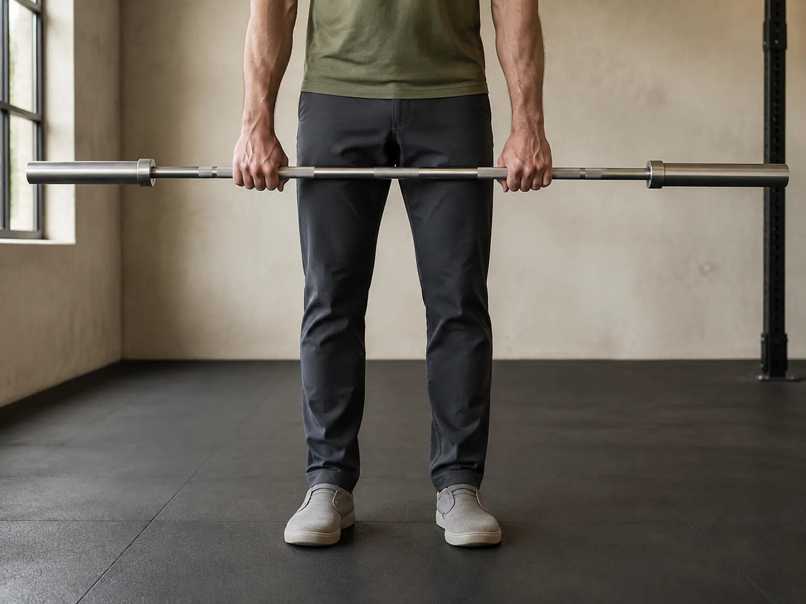 An athlete stands upright holding an unloaded straight bar in front of the upper thighs.